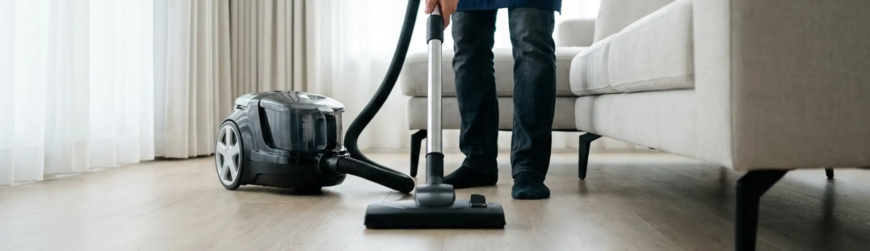 Professional house cleaner vacuuming a living room floor with a canister vacuum cleaner, Grand Rapids, MI.
