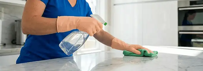 Maid service worker spraying and wiping a kitchen countertop with a microfiber cloth for sanitizing, Grand Rapids, MI.