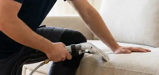 Professional upholstery cleaner deep-cleaning a fabric sofa with a handheld extraction tool, Grand Rapids, MI.