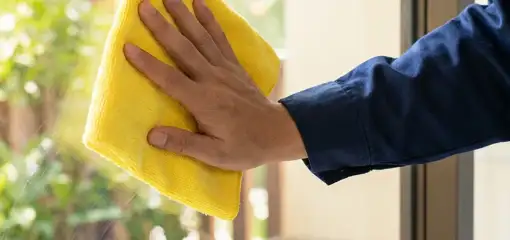 House cleaner wiping a glass window with a yellow microfiber cloth for streak-free cleaning, Grand Rapids, MI.